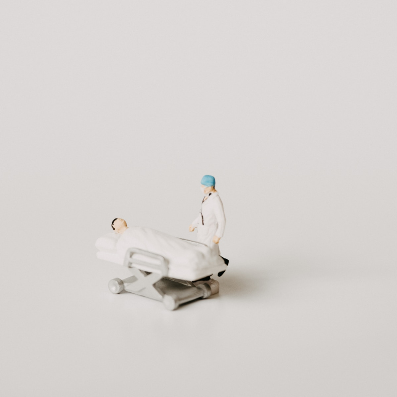 figurillas de ceramica miniaturade un paciente en camilla siendo atendido por un médico sobre fondo blanco